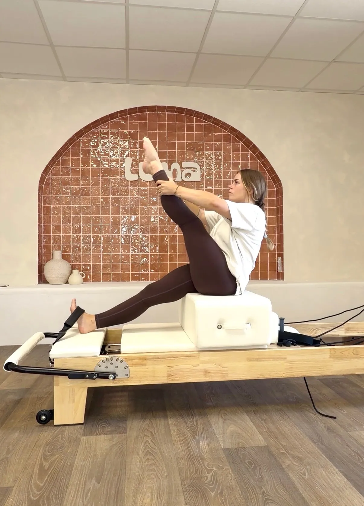 Inès Abellan, fondatrice de Luma Pilates Club, en exercice sur un Reformer devant l'arche en zellige du studio